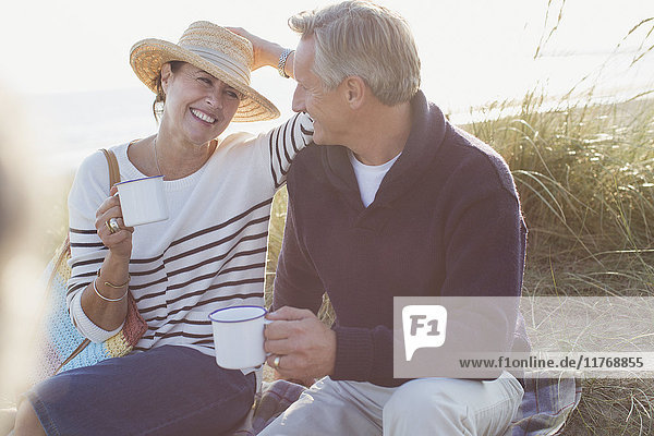 Mature couple drinking coffee in sunny beach grass