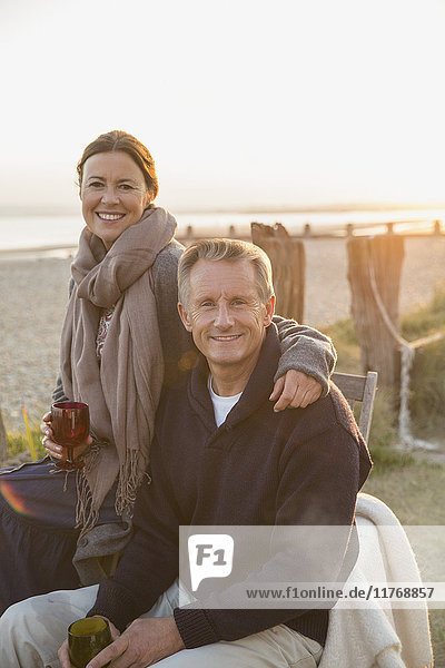 Portrait smiling mature couple drinking wine on sunset beach