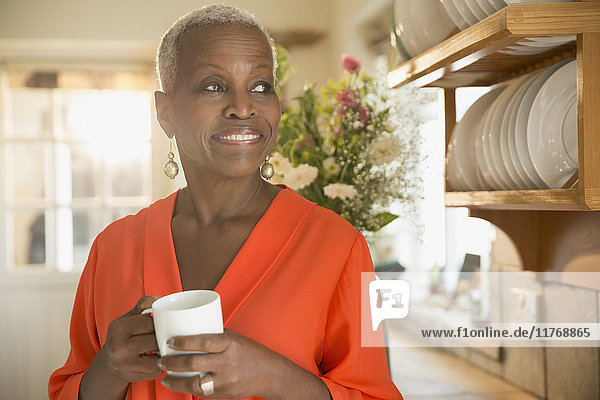 Lächelnde Seniorin beim Kaffeetrinken in der Küche