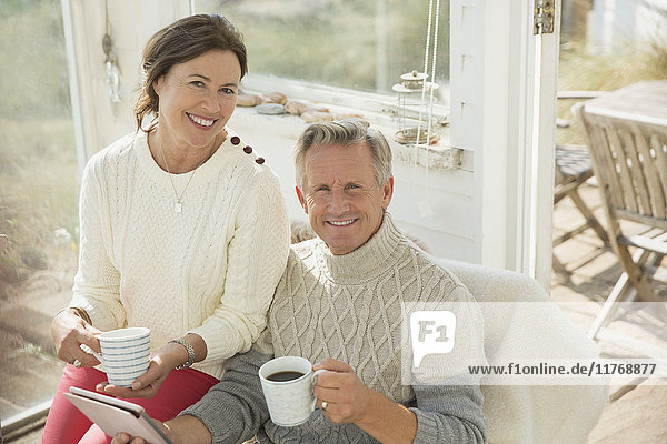 Portrait smiling mature couple using digital tablet and drinking coffee on sun porch