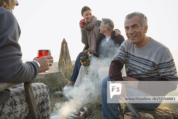 Mature couples drinking wine and barbecuing on beach