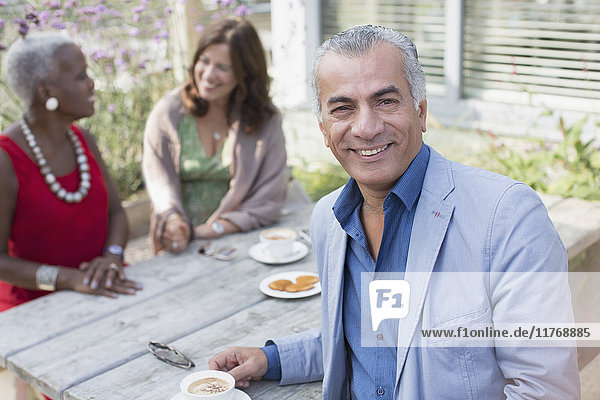 Portrait lächelnder älterer Mann beim Kaffeetrinken mit Freunden am Terrassentisch