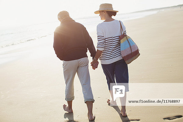 Barefoot mature couple holding hands and walking on sunny beach