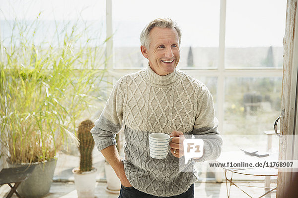 Lächelnder reifer Mann trinkt Kaffee am sonnigen Strand Haus Sonne Veranda