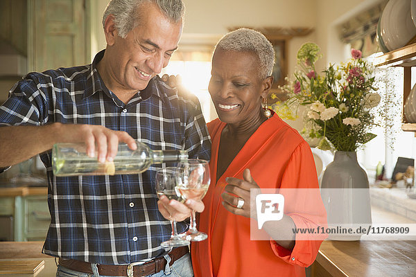 Lächelndes Seniorenpaar gießt Weißwein in die Küche