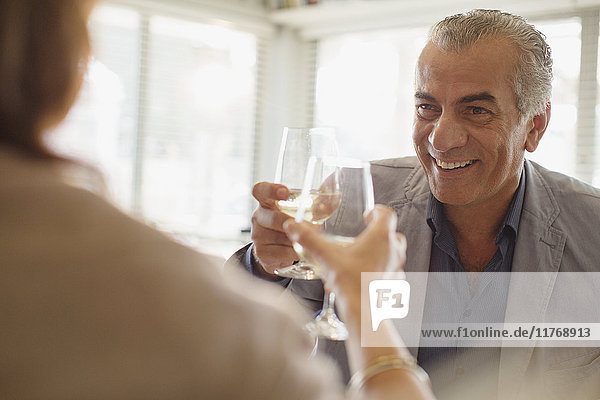 Lächelnder älterer Mann trinkt Wein  toastet Weingläser mit Frau im Restaurant