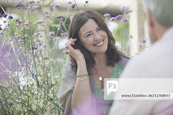 Lächelnde reife Frau im Gespräch mit dem Mann auf der Terrasse mit violetten Blumen