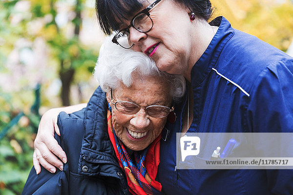 Caretaker embracing senior woman in park