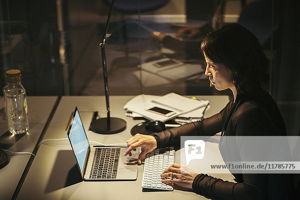 Hochwinkelansicht der Geschäftsfrau mit Laptop am Schreibtisch im Büro bei Nacht