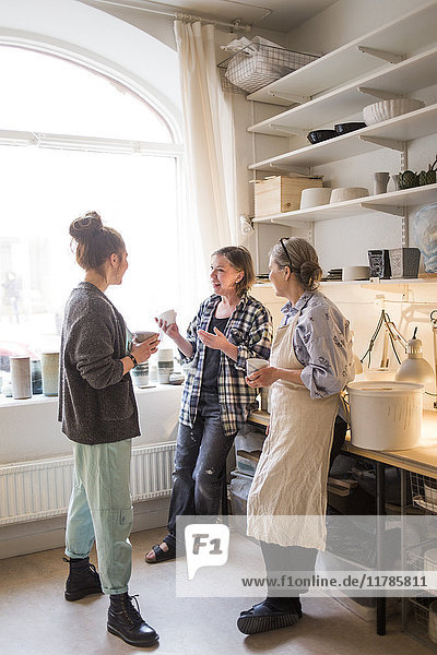 Happy female colleagues standing with coffee cups while talking at ceramics store