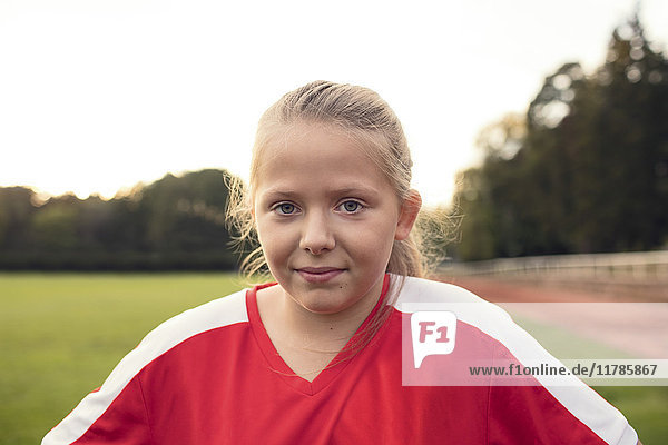 Porträt eines Mädchens in roter Uniform auf dem Fußballfeld gegen den Himmel stehend