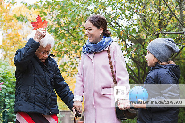 Mutter und Sohn sehen die ältere Frau mit dem Herbstblatt im Park.
