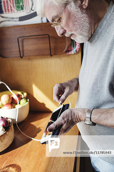 Seniorenkabel zum Handy an der Küchentheke an sonnigen Tagen