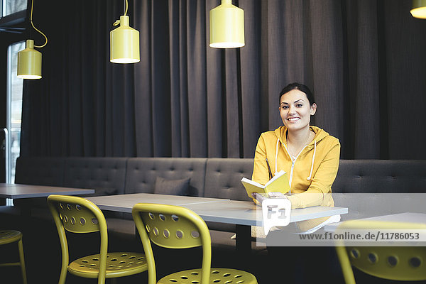 Porträt einer lächelnden mittelständischen Geschäftsfrau mit Buch in der Bürocafeteria