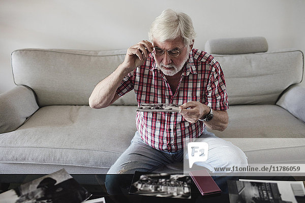 Älterer Mann schaut sich alte Fotos an  während er zu Hause auf dem Sofa sitzt.