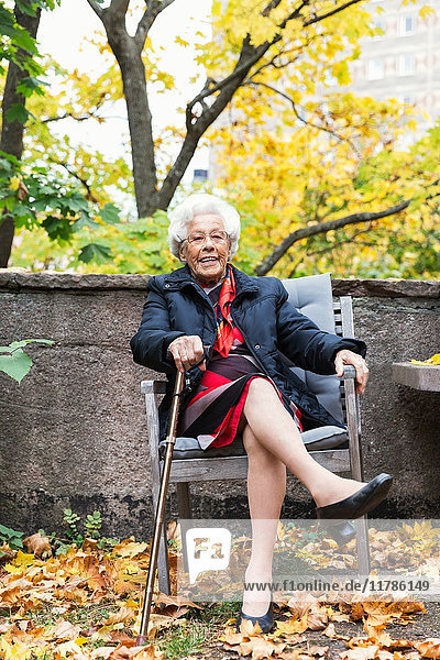Ganzkörperporträt einer glücklichen Seniorin auf einem Stuhl im Park