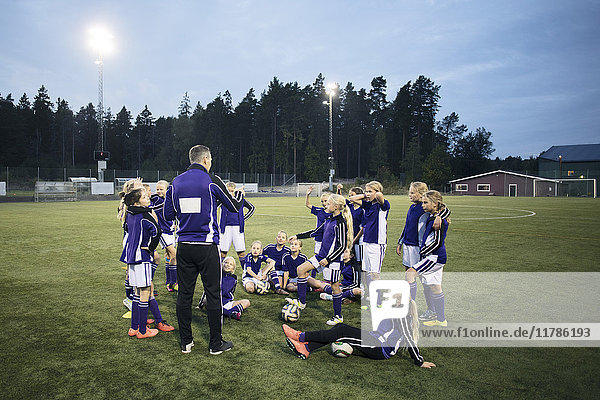 Coach erklärt mit Mädchen Fußballmannschaft auf dem Feld gegen den Himmel