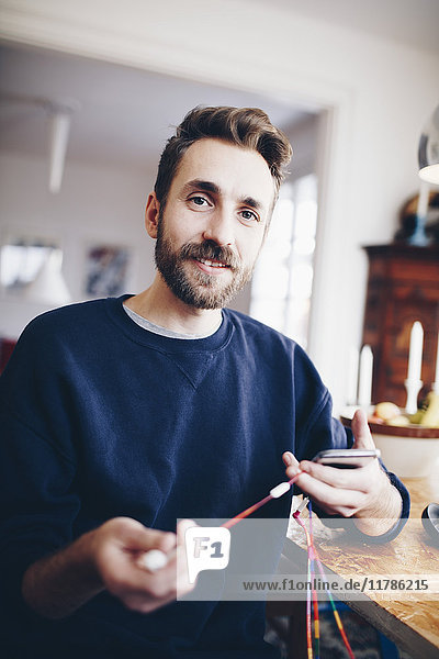 Porträt eines glücklichen Mannes mit Handy und Kopfhörer  der zu Hause am Tisch sitzt