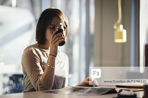 Geschäftsfrau beim Kaffeetrinken beim Lesen von Dokumenten am Schreibtisch im Büro
