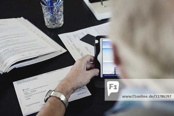 Abgeschnittenes Bild eines älteren Mannes  der beim Lesen von Rechnungen am Tisch ein digitales Tablett benutzt.