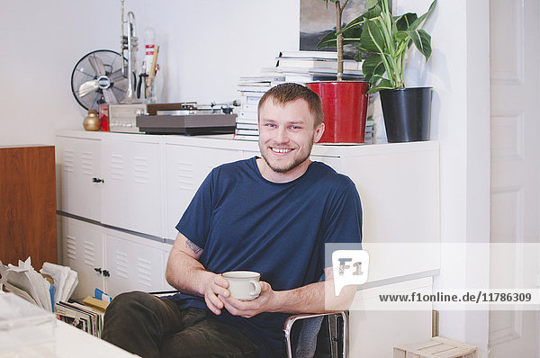 Portrait of happy businessman holding coffee cup while sitting in creative office