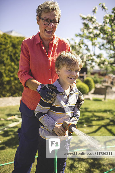 Glückliche Großmutter und Enkel spritzen Wasser im Hof
