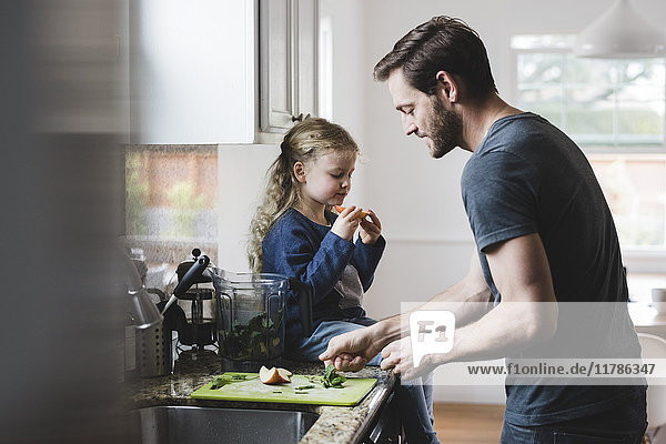 Seitenansicht des Vaters beim Kochen während die Tochter einen Apfel in der Küche hat.