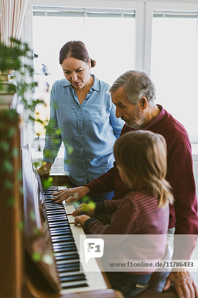 Frau sieht den Jungen und den Urgroßvater beim Klavierspielen an.