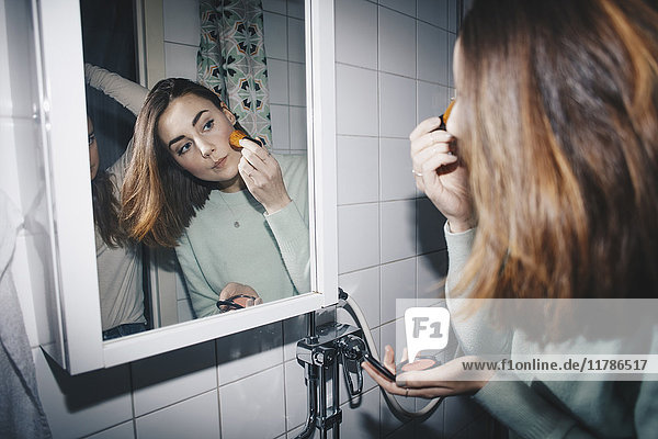 Junge Frau  die errötet  schaut in den Spiegel auf das College-Badezimmer.