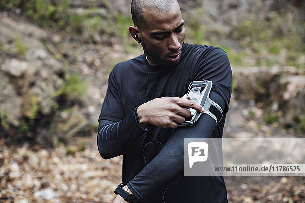 Männlicher Sportler mit Smartphone im Armband im Wald