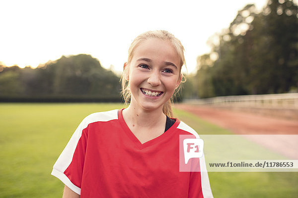 Fröhliches Mädchen in roter Sportuniform auf dem Fußballfeld gegen den Himmel stehend