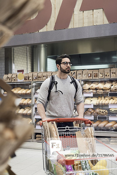 Mann schiebt Einkaufswagen mit Lebensmitteln gegen das Regal im Supermarkt