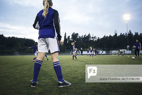Rückansicht des Mädchens mit Blick auf die Spieler  die auf dem Fußballplatz spielen.