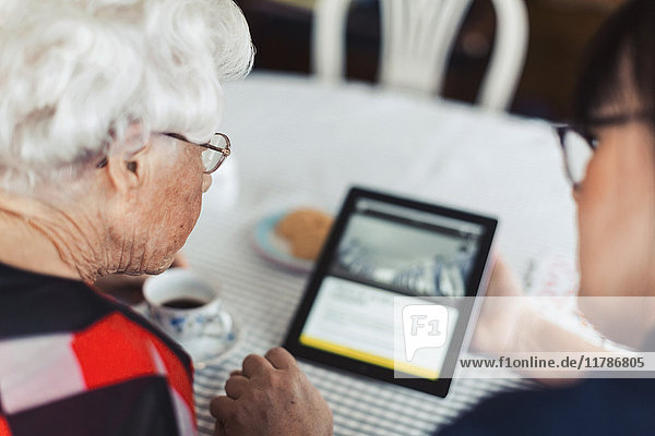 Hochwinkelansicht von Hausmeisterin und Seniorin mit digitalem Tablett zu Hause