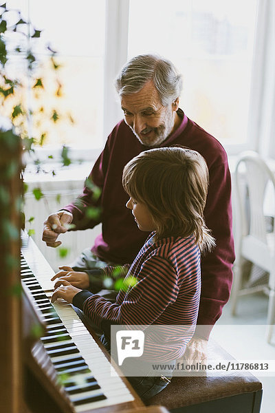 Happy senior man talking to great grandfather playing piano at home