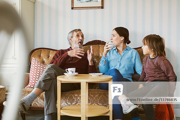 Senior Mann im Gespräch mit Tochter und Urenkel auf Sofa im Wohnzimmer