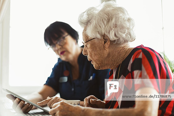 Seniorin mit digitalem Tablett und Betreuerin zu Hause