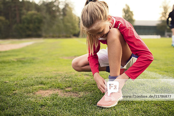 Mädchen kauernd beim Binden von Schnürsenkeln auf dem Fußballplatz