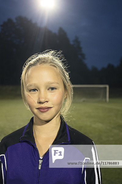 Porträt eines selbstbewussten Mädchens  das nachts auf dem Fußballfeld steht.