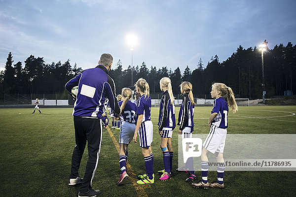 Coach explaining female soccer team on field against sky