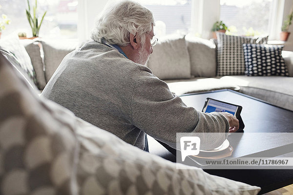 Senior Mann mit digitalem Tablett im Sitzen auf dem Sofa zu Hause