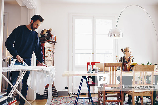 Man ironing while woman looking away in dining room at home