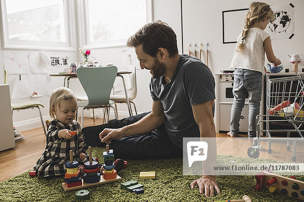 Vater und Töchter spielen mit Spielzeug im Spielzimmer zu Hause
