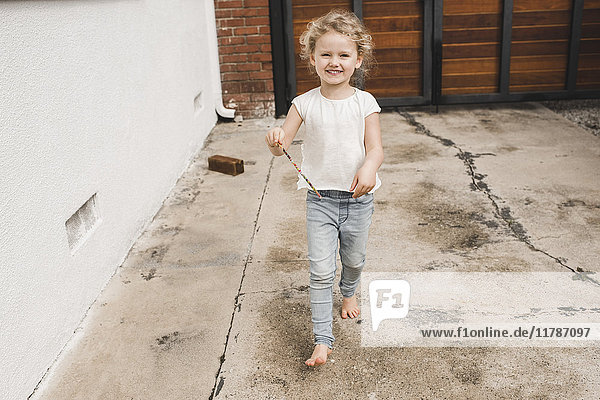 Porträt eines glücklichen Mädchens  das mit einem Zauberstab außerhalb des Hauses spielt.