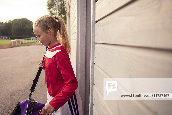 Side view of girl with bag standing by wall