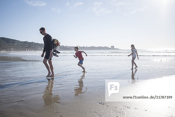 Full length of father with children enjoying vacation at beach on sunny day