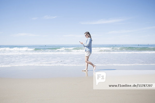 Vollständige Seitenansicht der reifen Frau mit dem Handy beim Spaziergang am Strand