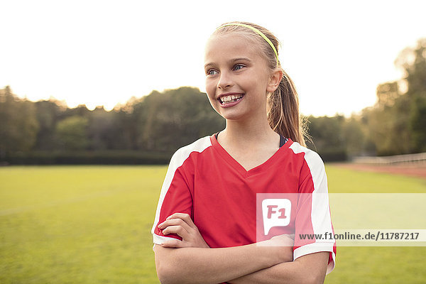 Happy female athlete looking away standing with arms crossed on soccer field