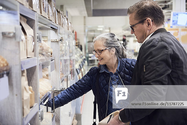Lächelnde Frau nimmt Essen aus dem Schrank  während sie mit dem Mann im Supermarkt steht.
