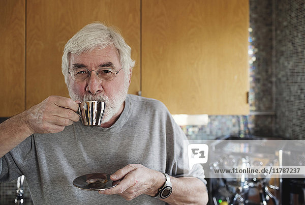 Porträt eines älteren Mannes  der Kaffee trinkt  während er in der Küche steht.